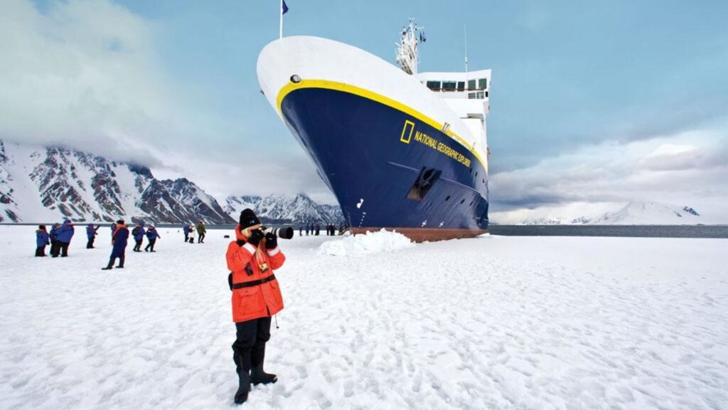 Traveler photographing an expedition cruise ship docked against Antarctic ice