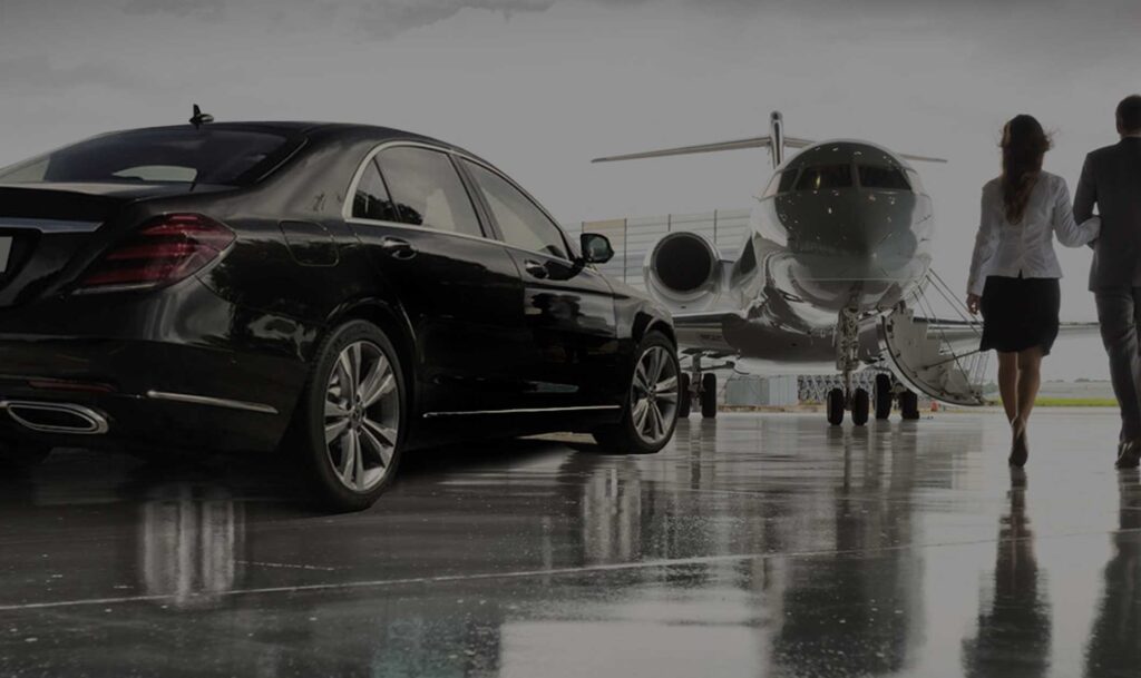 Black luxury sedan and travelers beside a private jet on a wet tarmac