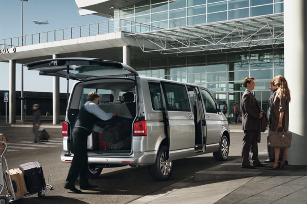 Driver loading luggage into a passenger van at an airport terminal