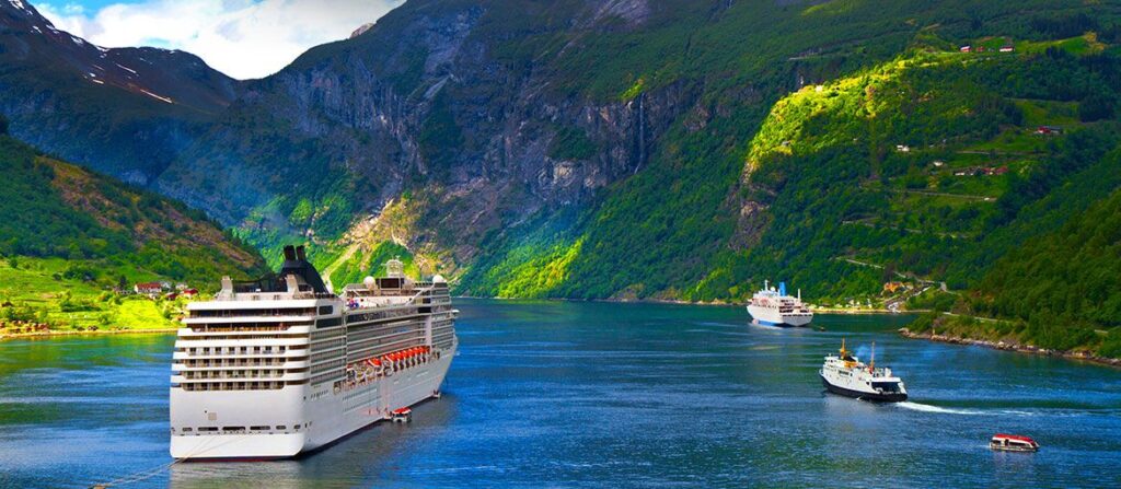 Cruise ship in a green Norwegian fjord with small boats nearby