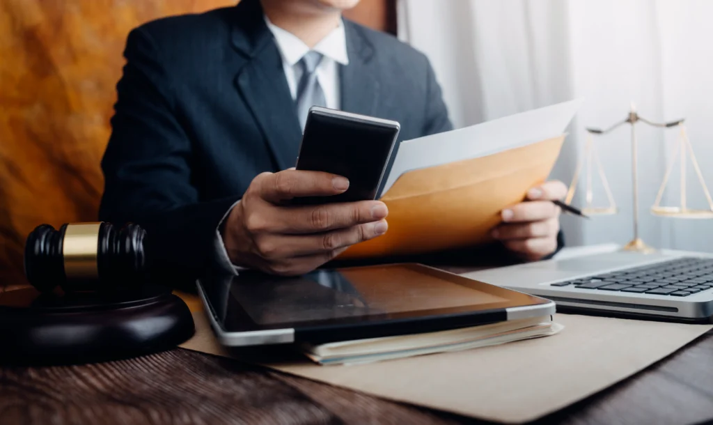 Businessman holding a phone and documents at a desk with a scale of justice
