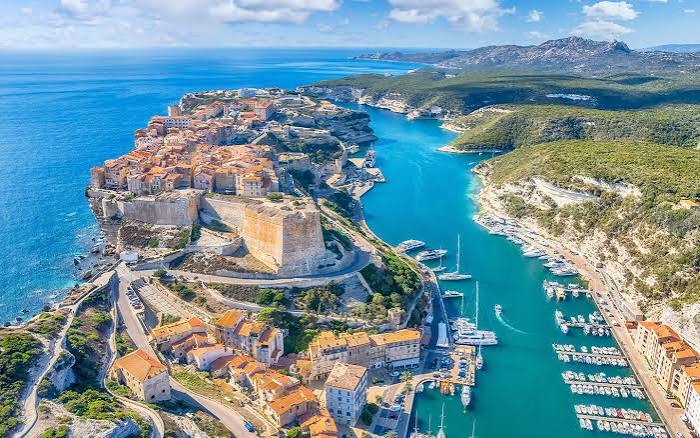 Aerial view of a cliffside Mediterranean town and harbor beside turquoise sea
