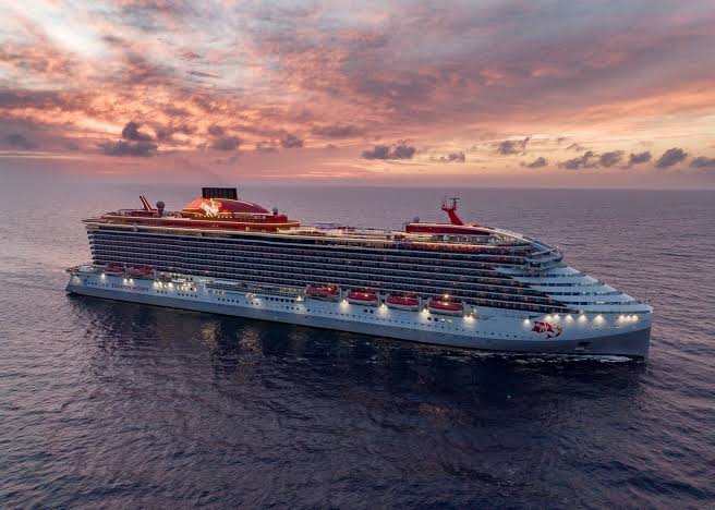 Virgin Voyages cruise ship sailing under a pink sunset sky