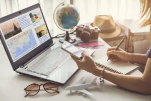 Person planning a vacation on a laptop with a globe, camera, hat and sunglasses